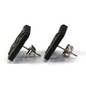 May include: A pair of black square stud earrings with a detailed design. The earrings have silver posts and butterfly backs.
