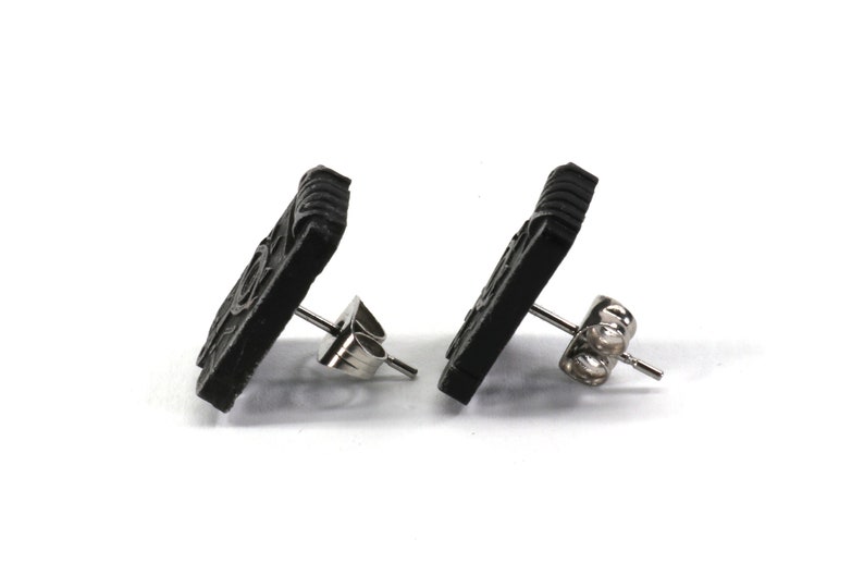 May include: A pair of black square stud earrings with a detailed design. The earrings have silver posts and butterfly backs.