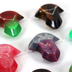 May include: Assortment of colourful resin arrowhead-shaped dice with a constellation design. The dice are translucent and show a white constellation design inside.