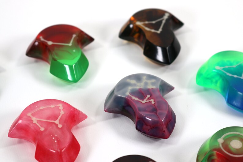 May include: Assortment of colourful resin arrowhead-shaped dice with a constellation design. The dice are translucent and show a white constellation design inside.