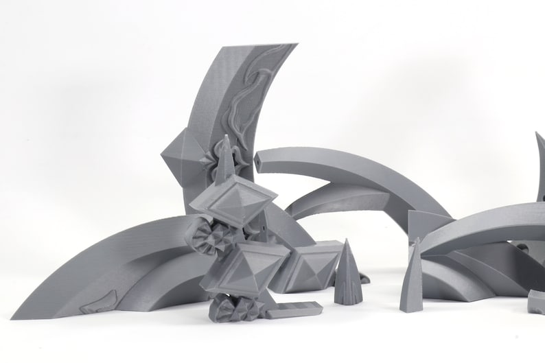 May include: A set of gray 3D printed geometric shapes, including arches, points, and pyramids. The shapes are arranged in a random pattern on a white surface.