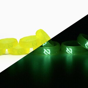 May include: A set of six glow-in-the-dark dice with a yellow color and white numbers. The dice are shown in a white background and a black background to show how they glow in the dark.