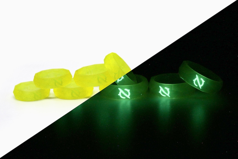 May include: A set of six glow-in-the-dark dice with a yellow color and white numbers. The dice are shown in a white background and a black background to show how they glow in the dark.