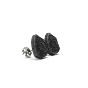 May include: A pair of black metal stud earrings featuring a shield design. The shield has a detailed design and is slightly raised from the earring base.