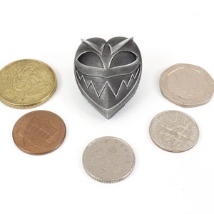 May include: A silver heart-shaped pendant with a menacing face and sharp teeth. The pendant is surrounded by six coins.