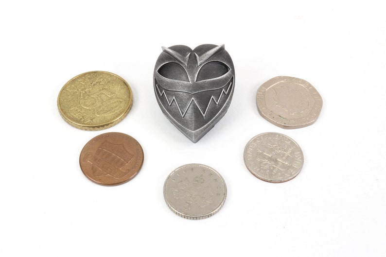 May include: A silver heart-shaped pendant with a menacing face and sharp teeth. The pendant is surrounded by six coins.