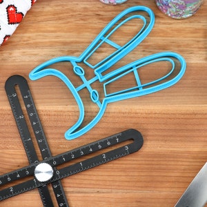 May include: A blue plastic bunny cookie cutter on a wooden surface with a black measuring tool and a blue spatula.