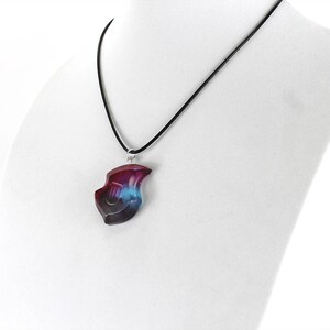 May include: A black cord necklace with a pendant shaped like a lyre. The pendant is made of resin and has a blue, purple, and pink color scheme.