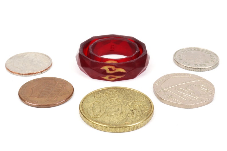 May include: A red, faceted ring with a yellow flame design. The ring is surrounded by six coins.