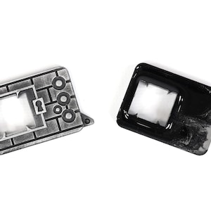 May include: Two metal keychains, one silver and one black. The silver keychain is shaped like a brick wall with a keyhole and three circles. The black keychain is a simple rectangle with a square cutout.