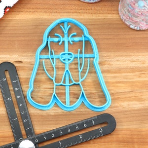 May include: A blue plastic cookie cutter shaped like a Bloodhound dog. The cutter is on a wooden surface.