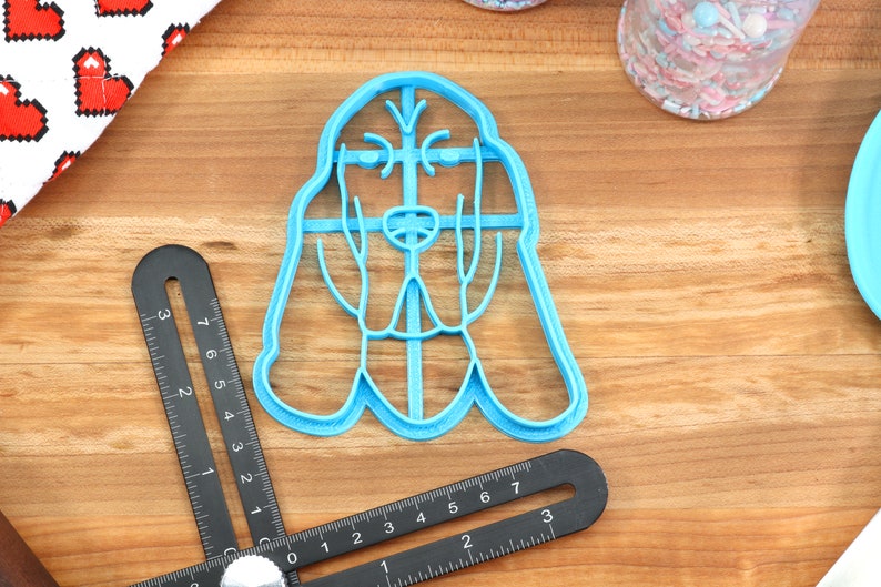 May include: A blue plastic cookie cutter shaped like a Bloodhound dog. The cutter is on a wooden surface.