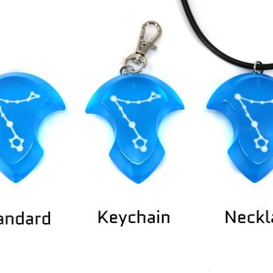 K&ouml;nnte beinhalten: Drei Versionen eines blauen Anh&auml;ngers mit einem wei&szlig;en Sternbild-Design. Der Anh&auml;nger ist als Standardst&uuml;ck, als Schl&uuml;sselanh&auml;nger und als Halskette erh&auml;ltlich.