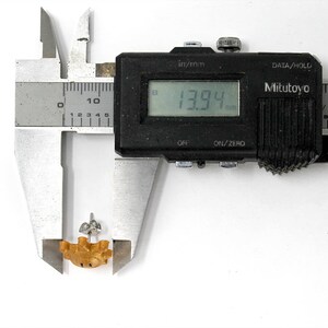 May include: A digital caliper measuring a small, brown, ceramic object. The caliper reads 13.94 mm.