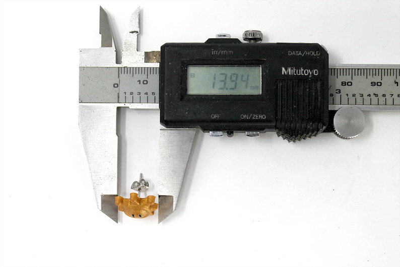 May include: A digital caliper measuring a small, brown, ceramic object. The caliper reads 13.94 mm.