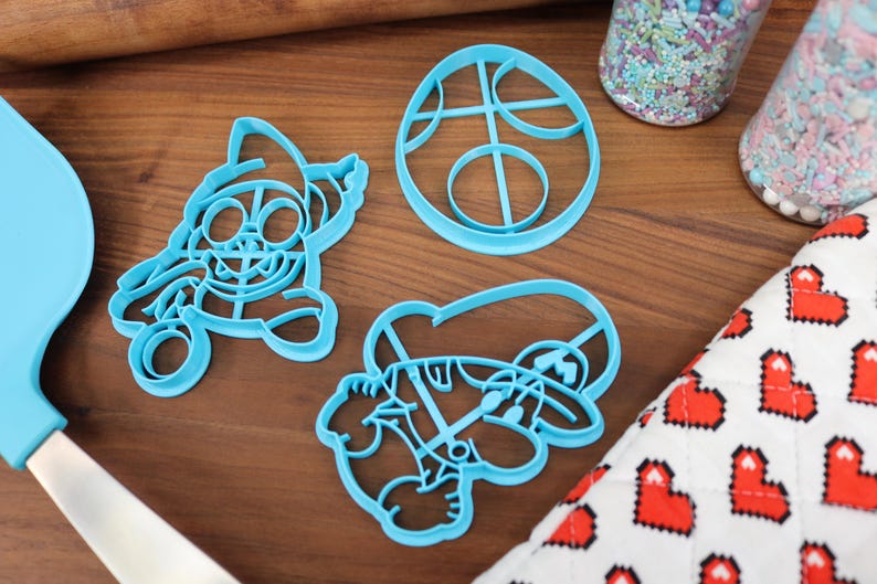 Op de afbeelding: Drie blauwe plastic koekjesvormen in de vorm van een videogamepersonage, een videogamepersonage met een hoed en een cirkel met een ontwerp erin.