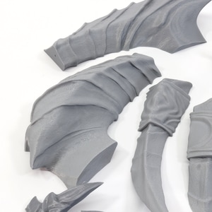 Pode incluir: Um conjunto de asas, garras e pe&ccedil;as de cauda de drag&atilde;o impressas em 3D na cor cinza. As pe&ccedil;as s&atilde;o detalhadas e texturizadas, com uma apar&ecirc;ncia escamosa.