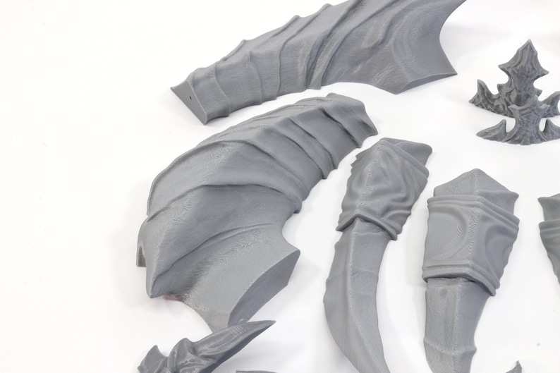 Pode incluir: Um conjunto de asas, garras e pe&ccedil;as de cauda de drag&atilde;o impressas em 3D na cor cinza. As pe&ccedil;as s&atilde;o detalhadas e texturizadas, com uma apar&ecirc;ncia escamosa.