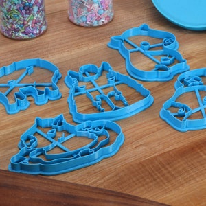 May include: Five blue plastic cookie cutters shaped like animals. The cutters are on a wooden surface.