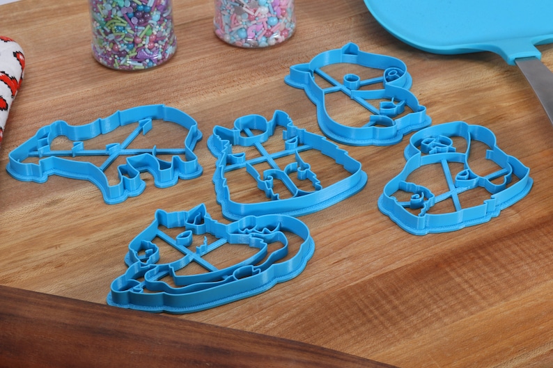 May include: Five blue plastic cookie cutters shaped like animals. The cutters are on a wooden surface.