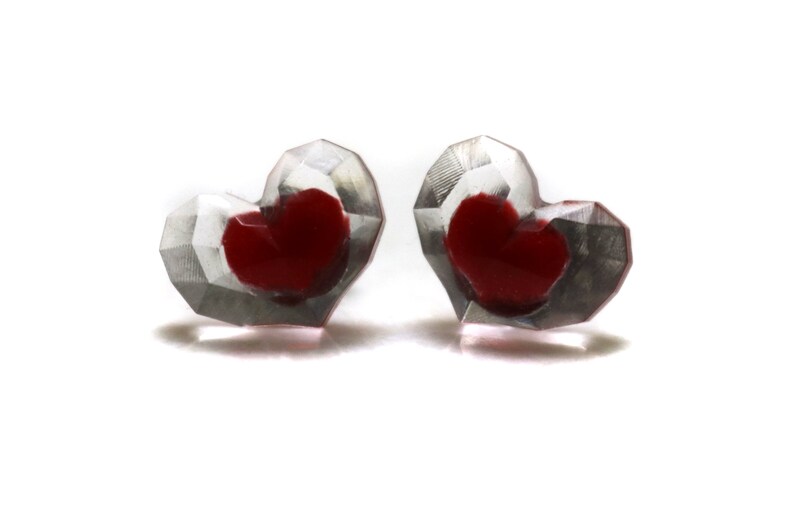 Puede incluir: Un par de pendientes en forma de coraz&oacute;n con un dise&ntilde;o transparente facetado. Cada pendiente tiene un coraz&oacute;n rojo en el interior.