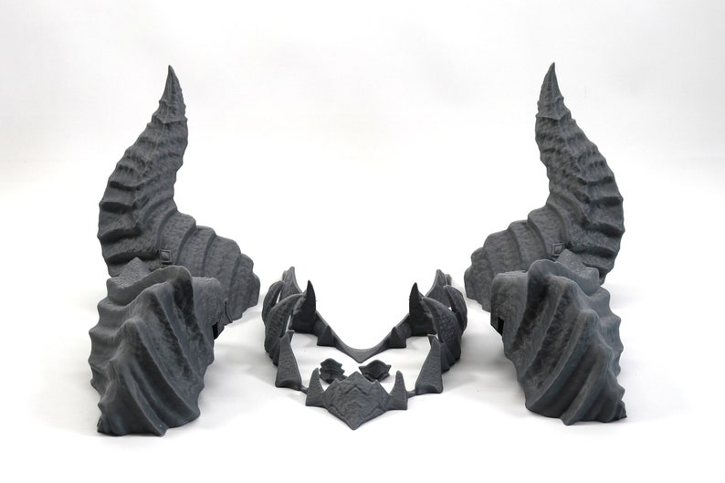 May include: A set of three gray 3D printed horns, two large horns and a smaller piece that connects them. The horns are detailed with a textured, scaly surface.