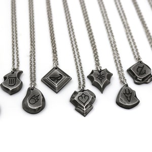 Pode incluir: Um conjunto de 10 colares de prata com diferentes pingentes que apresentam v&aacute;rios s&iacute;mbolos e designs. Os pingentes s&atilde;o todos em um estilo semelhante, com uma superf&iacute;cie &aacute;spera e texturizada. Os colares est&atilde;o todos em um fundo branco.