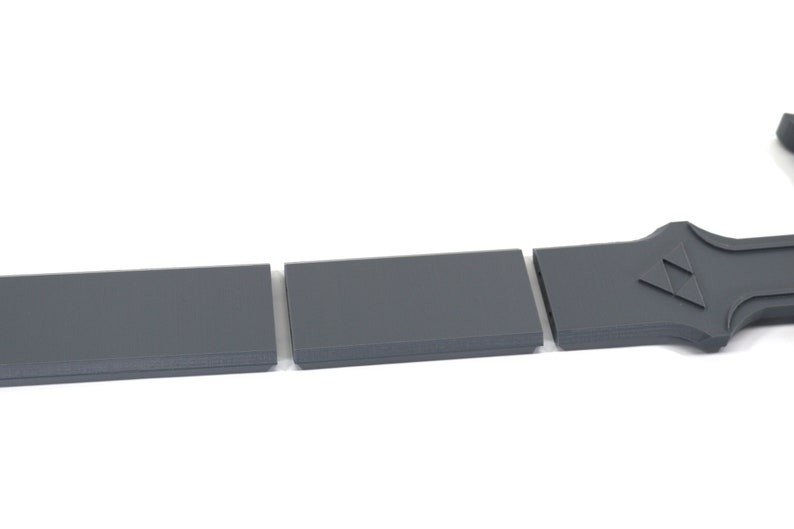 Puede incluir: Tres piezas de pl&aacute;stico gris que se pueden ensamblar para formar una espada. La espada tiene un dise&ntilde;o triangular en el mango.
