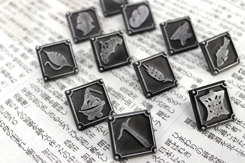 May include: A set of ten silver-toned metal pins with different designs. Each pin is square-shaped and features a different design, including a leaf, a wheat stalk, a pickaxe, and a creature.