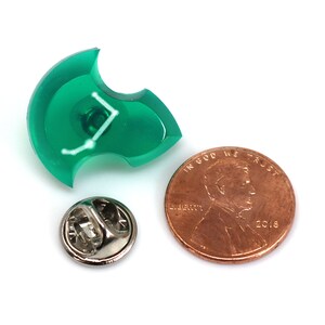 Puede incluir: Un pin de pl&aacute;stico verde con un dise&ntilde;o de constelaci&oacute;n blanca. El pin es del tama&ntilde;o de una moneda de un centavo de d&oacute;lar estadounidense.