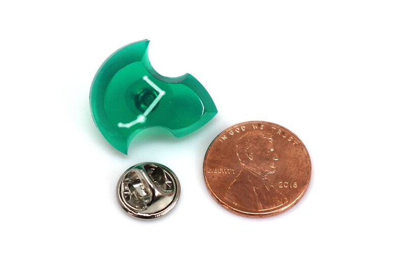 Puede incluir: Un pin de pl&aacute;stico verde con un dise&ntilde;o de constelaci&oacute;n blanca. El pin es del tama&ntilde;o de una moneda de un centavo de d&oacute;lar estadounidense.