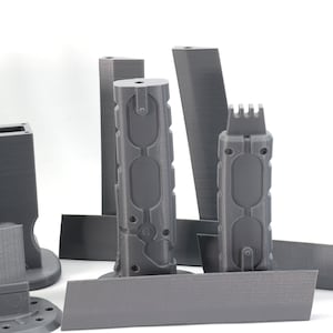 Puede incluir: Un conjunto de piezas grises impresas en 3D para una pistola de modelo. Las piezas incluyen un ca&ntilde;&oacute;n, una empu&ntilde;adura, un cargador y una mira.
