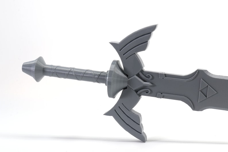 Puede incluir: Una r&eacute;plica de pl&aacute;stico gris de la Espada Maestra de la serie de videojuegos The Legend of Zelda. La espada tiene una empu&ntilde;adura detallada y una hoja triangular con el s&iacute;mbolo de la Trifuerza.