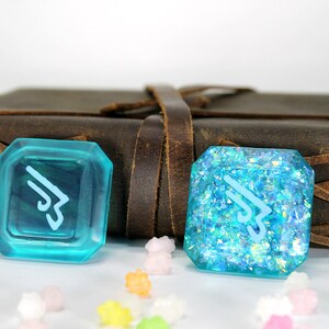 May include: Two turquoise blue resin dice with a white symbol on each. The dice are on a brown leather surface with a white background.