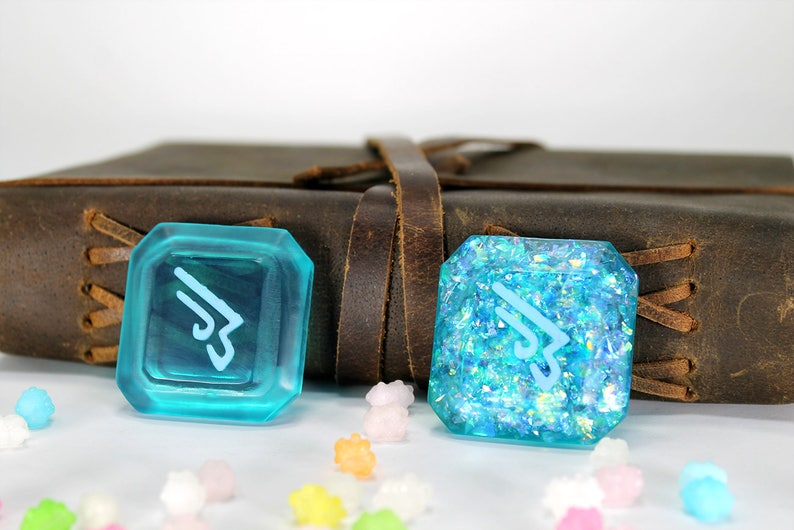 May include: Two turquoise blue resin dice with a white symbol on each. The dice are on a brown leather surface with a white background.