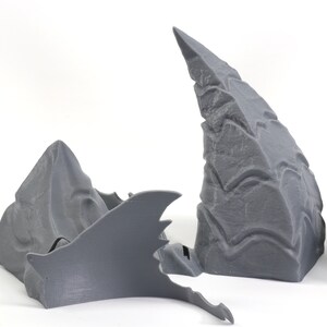 Op de afbeelding: Drie grijze 3D-geprinte onderdelen, twee zijn hoog en puntig, en &eacute;&eacute;n is plat en vleugelvormig.