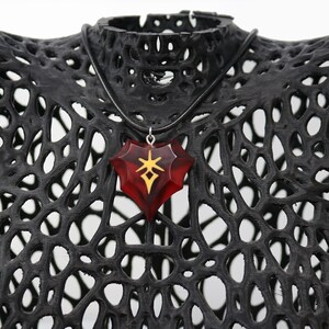 May include: A red heart-shaped pendant necklace with a gold symbol inside. The necklace is on a black mannequin bust.