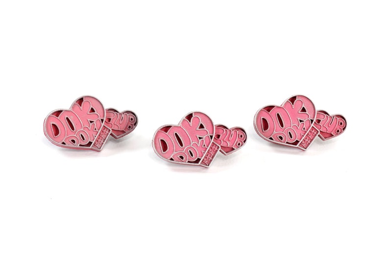 May include: Three pink heart-shaped pins with the text "DOKI DOKI CLUB" on them.