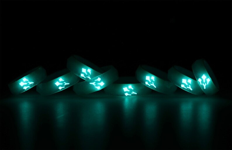 May include: A group of eight glow-in-the-dark silicone rings stacked on top of each other. The rings are a light teal color and have a geometric design.