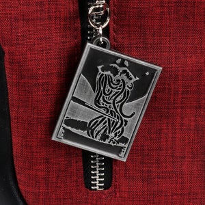 May include: A silver zipper pull with a detailed design of a creature with tentacles. The zipper pull is attached to a red fabric bag.