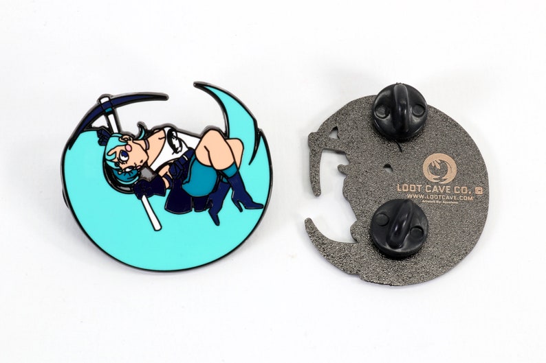 May include: A teal blue enamel pin featuring a cartoon character holding a pickaxe, sitting on a crescent moon. The back of the pin is silver with the text "Loot Cave Co.  www.lootcave.com" and two black butterfly clasps.