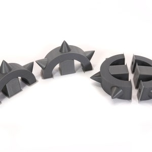 May include: Three grey plastic pieces with spikes, each shaped like a half-circle, designed to be assembled into a circle.