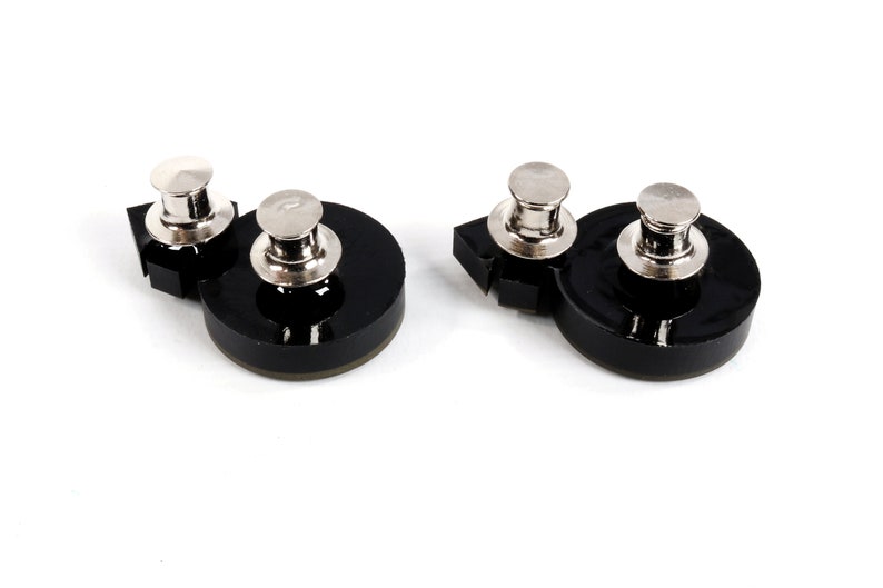 May include: Two black plastic bases with silver metal push pins. The bases are round with a slightly raised edge. The push pins are cylindrical with a flat top.