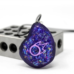 May include: A purple pendant necklace with a pink fire symbol inside. The pendant is made of resin and has a glittery finish.
