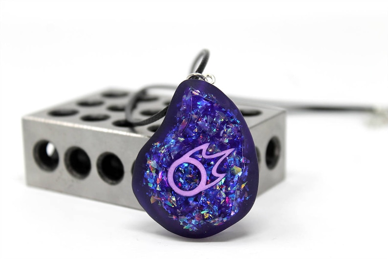 May include: A purple pendant necklace with a pink fire symbol inside. The pendant is made of resin and has a glittery finish.