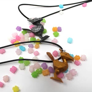 May include: Two necklaces with black cords and pendant charms. One charm is a silver-colored bird, the other is a gold-colored bird. The necklaces are surrounded by colorful candy-like sprinkles.