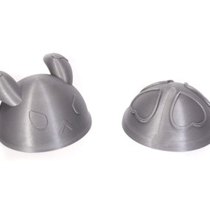 Op de afbeelding: Twee 3D-geprinte grijze plastic hoeden in de vorm van een konijn. De ene hoed is geassembleerd, de andere is gedemonteerd en laat de twee delen zien waaruit de hoed bestaat.
