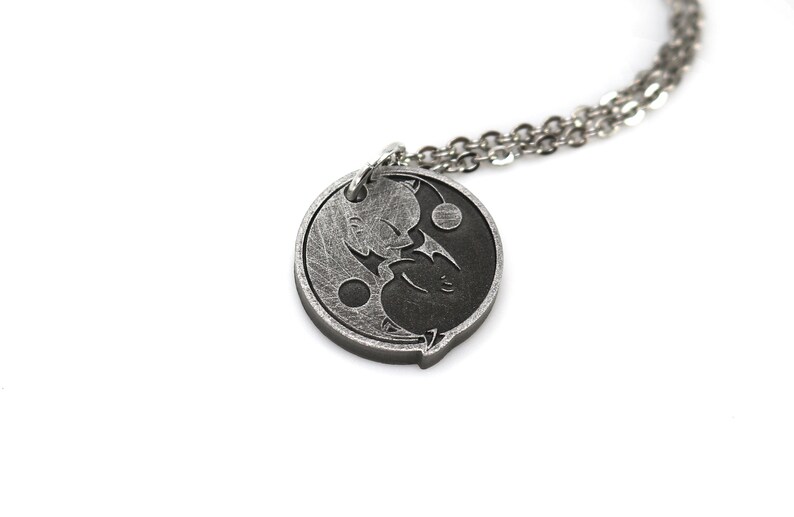 May include: A silver necklace with a yin yang pendant featuring two cartoon characters. The pendant is round and has a textured surface.