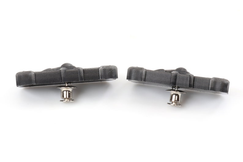 May include: Two black brake pads with silver metal pins. The brake pads are designed for bicycles.