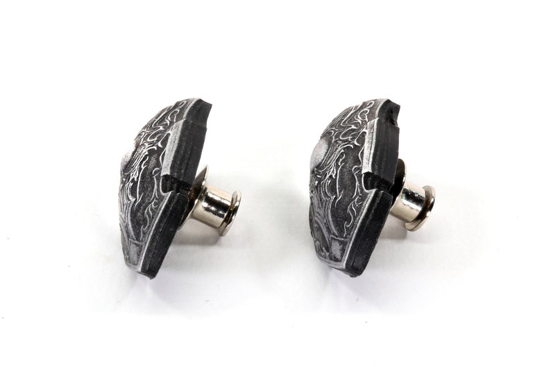 May include: Two black and silver bicycle toe clips with a decorative design. The toe clips are attached to a metal post.